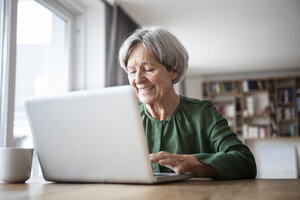 Porträt einer älteren Frau, die zu Hause einen Laptop benutzt - RBF004179