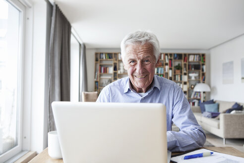 Porträt eines älteren Mannes, der mit einem Laptop am Tisch im Wohnzimmer sitzt - RBF004183