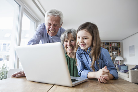 Großeltern und ihre Enkelin haben Spaß mit dem Laptop zu Hause, lizenzfreies Stockfoto