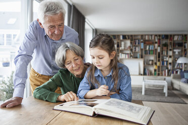 Grandparents watching photo album with their granddaughter at home - RBF004197