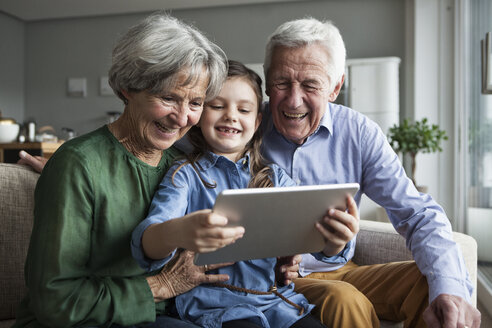Großeltern und ihre Enkelin sitzen zusammen auf der Couch und schauen auf ein digitales Tablet - RBF004204