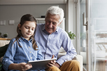 Grandfather and his granddaughter sitting together on the couch using digital tablet - RBF004205