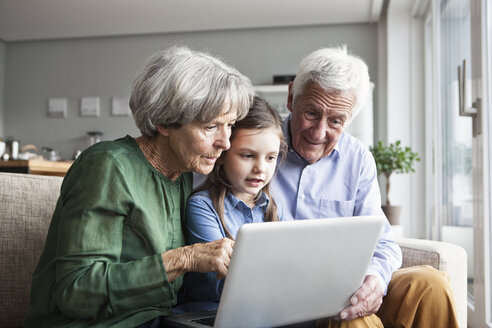Großeltern und ihre Enkelin sitzen zusammen auf der Couch und schauen auf ein digitales Tablet - RBF004206