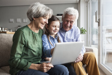 Großeltern und ihre Enkelin sitzen zusammen auf der Couch und schauen auf ein digitales Tablet - RBF004207