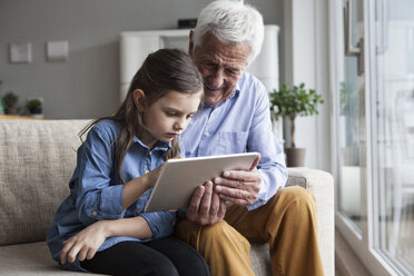 Grandfather and his granddaughter sitting together on the couch using digital tablet - RBF004208