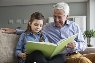 Großvater und seine Enkelin sitzen zusammen auf der Couch mit einem Buch - RBF004210