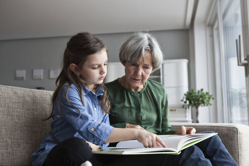 Großmutter und ihre Enkelin sitzen zusammen auf der Couch mit einem Buch - RBF004211