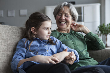 Grandmother and her granddaughter sitting together on the couch at home - RBF004213