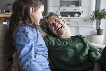 Lachende Großmutter und ihre Enkelin auf der Couch zu Hause - RBF004215