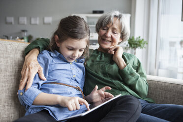 Großmutter und ihre Enkelin sitzen zusammen auf der Couch mit digitalem Tablet - RBF004220