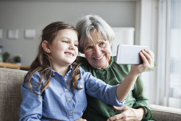 Großmutter und ihre Enkelin sitzen zusammen auf der Couch und machen ein Selfie mit dem Smartphone - RBF004221