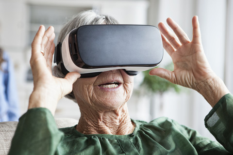 Ältere Frau benutzt Virtual-Reality-Brille zu Hause, lizenzfreies Stockfoto