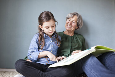 Happy grandmother and her granddaughter sitting on the floor with a book - RBF004225