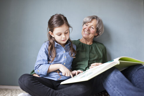 Glückliche Großmutter und ihre Enkelin sitzen mit einem Buch auf dem Boden - RBF004225