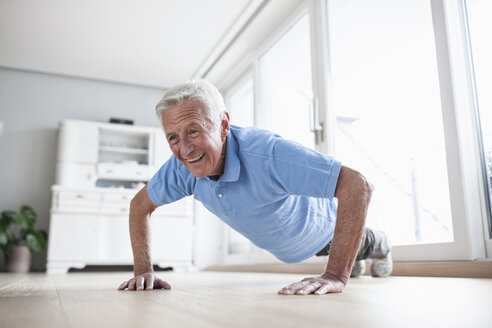 Portrait of senior man doing pushups at home - RBF004227