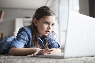 Porträt eines staunenden kleinen Mädchens, das mit einem Laptop auf dem Boden liegt - RBF004229