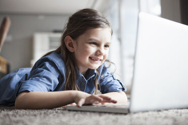 Porträt eines lächelnden kleinen Mädchens, das auf dem Boden liegt und einen Laptop benutzt - RBF004230