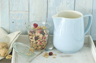 Glass of granola with dried blueberries and raspberries and a milk jug - ASF005853