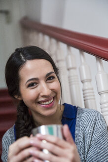 Porträt einer lächelnden Frau im Treppenhaus, die eine Tasse Kaffee hält - FKF001686