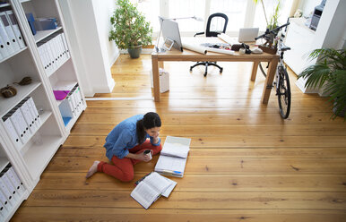 Woman sitting on the floor reading documents - FKF001693