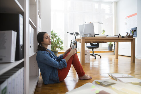 Frau sitzt auf dem Boden im Büro und macht eine Pause - FKF001694