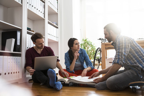 Drei kreative Geschäftsleute sitzen auf dem Boden und diskutieren, lizenzfreies Stockfoto