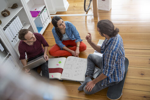 Drei kreative Geschäftsleute sitzen auf dem Boden und diskutieren - FKF001697