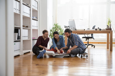 Three creative business people sitting on the floor looking in folder - FKF001699