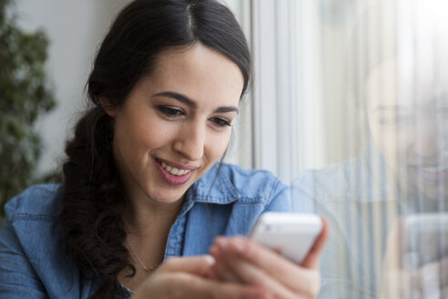 Lächelnde junge Frau schaut auf ihr Handy - FKF001706