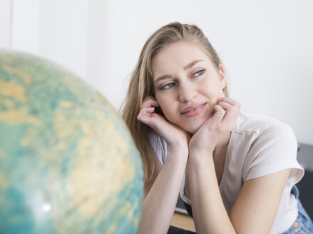 Porträt einer träumenden jungen Frau mit dem Kopf in den Händen neben einem Globus - FMKF002512