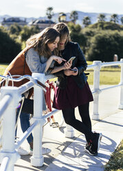 Zwei junge Frauen im Freien schauen auf ihr Handy - MGOF001480