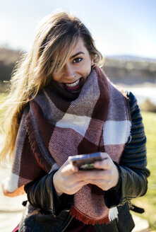 Porträt einer lächelnden jungen Frau mit Smartphone im Freien - MGOF001485