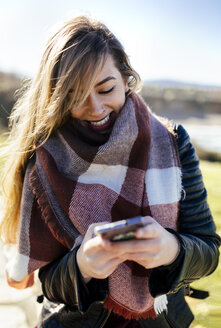 Lächelnde junge Frau benutzt Smartphone im Freien - MGOF001486