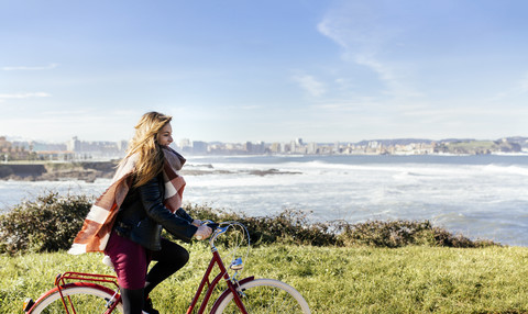 Spanien, Gijon, lächelnde junge Frau beim Fahrradfahren an der Küste, lizenzfreies Stockfoto