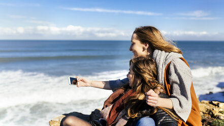 Spain, Gijon, two young women having fun with a smartphone near the sea - MGOF001497