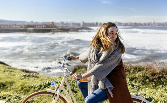 Spanien, Gijon, glückliche junge Frau beim Fahrradfahren an der Küste - MGOF001504