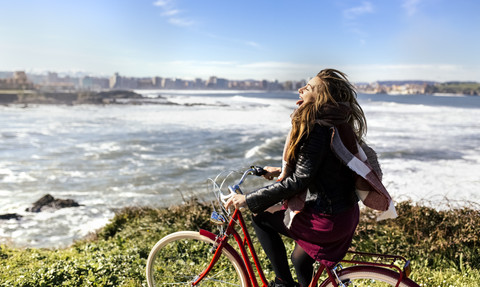 Spain, Gijon, playful young woman riding bicycle at the coast stock photo