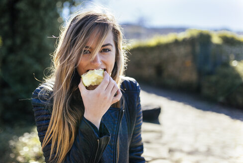 Porträt einer jungen Frau, die draußen einen Apfel isst - MGOF001513