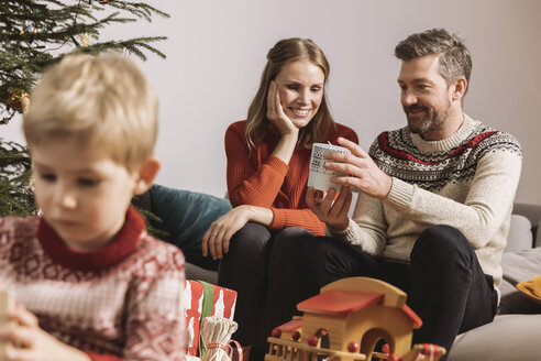 Eltern tauschen auf dem Sofa ein Weihnachtsgeschenk aus - MFF002753