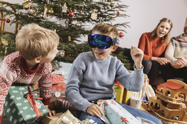 Brothers looking at new ski googles in front of Christmas tree - MFF002758