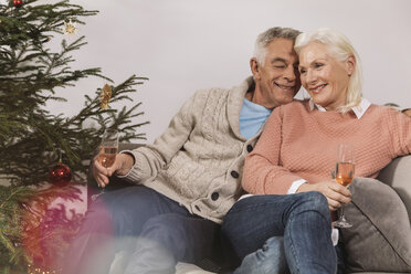 Senior couple sitting by Christmas tree drinking champagne - MFF002768