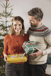 Ehepaar mit Weihnachtsgeschenken vor dem Baum stehend - MFF002780