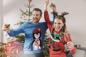 Zwei Personen mit hässlichen Weihnachtspullovern tanzen vor einem Baum - MFF002783