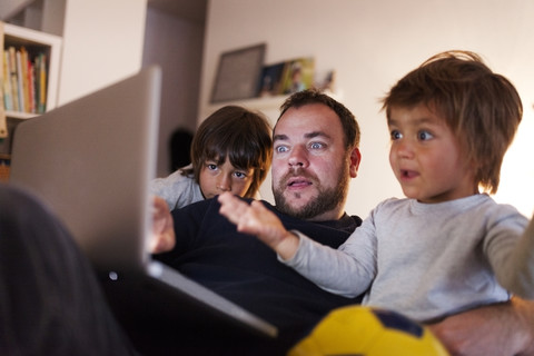 Vater und seine beiden kleinen Söhne sehen sich zu Hause ein Video auf dem Laptop an, lizenzfreies Stockfoto