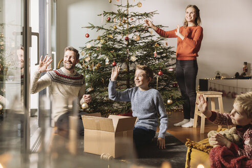 Familie schmückt Weihnachtsbaum, winkt aus dem Fenster - MFF002799