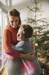 Glückliche Mutter und Sohn umarmen sich am Weihnachtsbaum - MFF002815