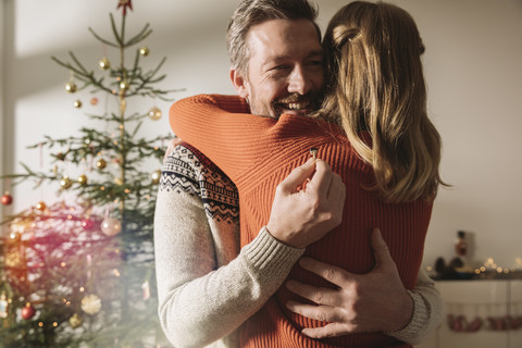 Paar umarmt sich nach Verlobung am Weihnachtsbaum, lizenzfreies Stockfoto