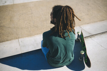 Rückenansicht eines jungen Mannes mit Dreadlocks, der in einem Skatepark sitzt - KIJF000236