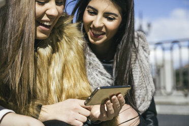 Zwei glückliche Frauen schauen auf ihr Smartphone - ABZF000266