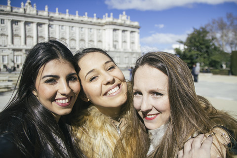 Spanien, Madrid, drei glückliche Frauen machen ein Selfie vor dem Königspalast, lizenzfreies Stockfoto